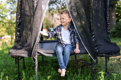 Photo of Happy little boy sitting on black trampoline outdoors