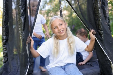 Photo of Happy little girl and her friends on black trampoline outdoors