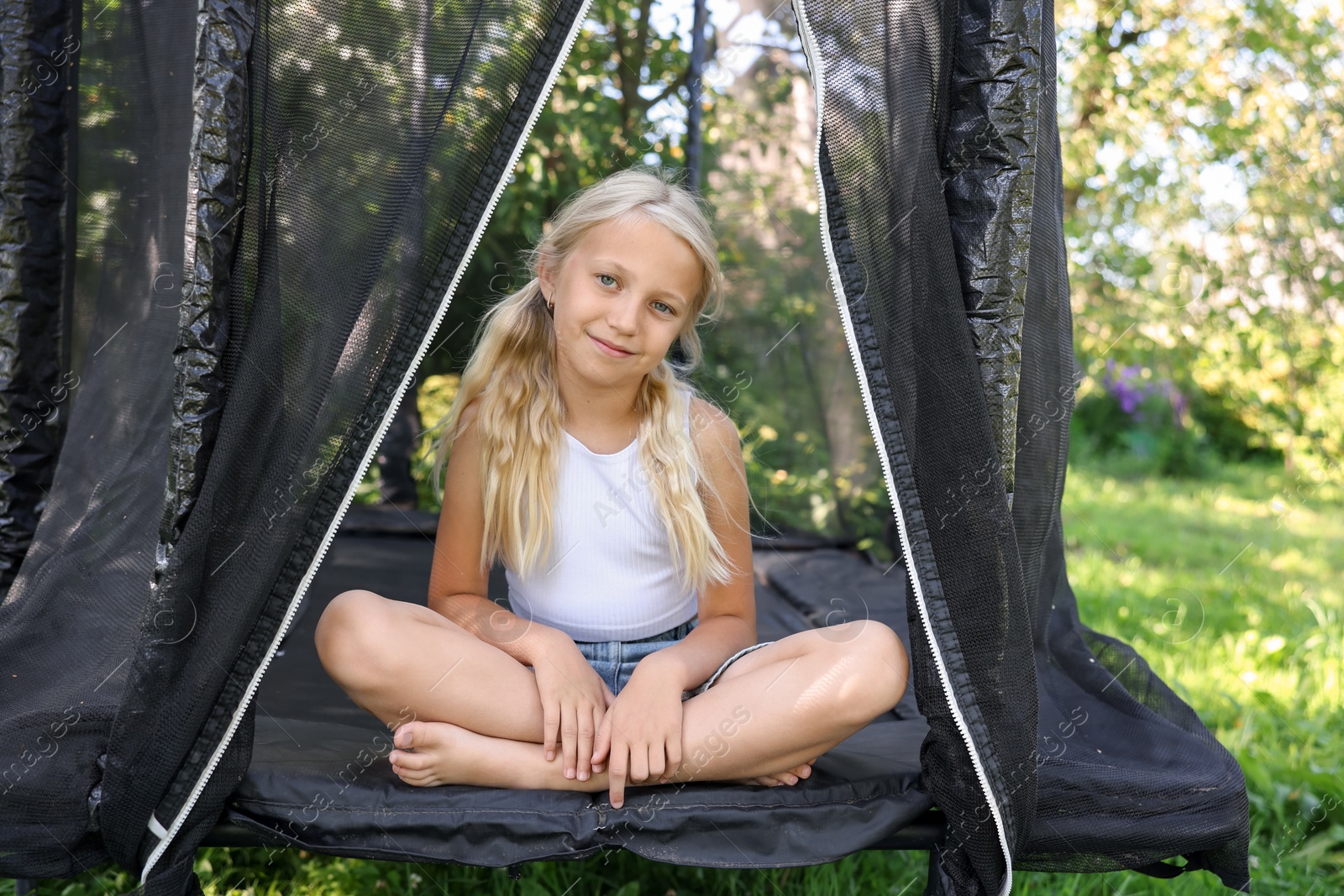 Photo of Cute little girl sitting on black trampoline outdoors
