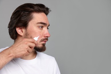 Photo of Young man with acne problem applying cream onto his face on light grey background. Space for text