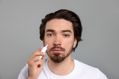 Photo of Young man with acne problem applying cream onto his face on light grey background