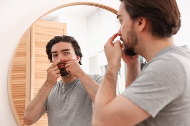 Photo of Young man with acne problem near mirror at home