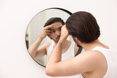 Photo of Young man with acne problem near mirror at home