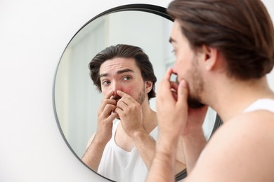 Photo of Young man with acne problem near mirror at home