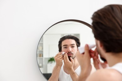 Photo of Young man with acne problem applying cream onto his face near mirror at home, space for text