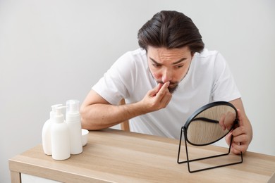 Photo of Young man with acne problem looking at mirror at table indoors