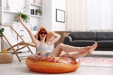 Photo of Happy woman in sunglasses and straw hat with inflatable ring having fun on floor at home. Dreaming about vacation at sea