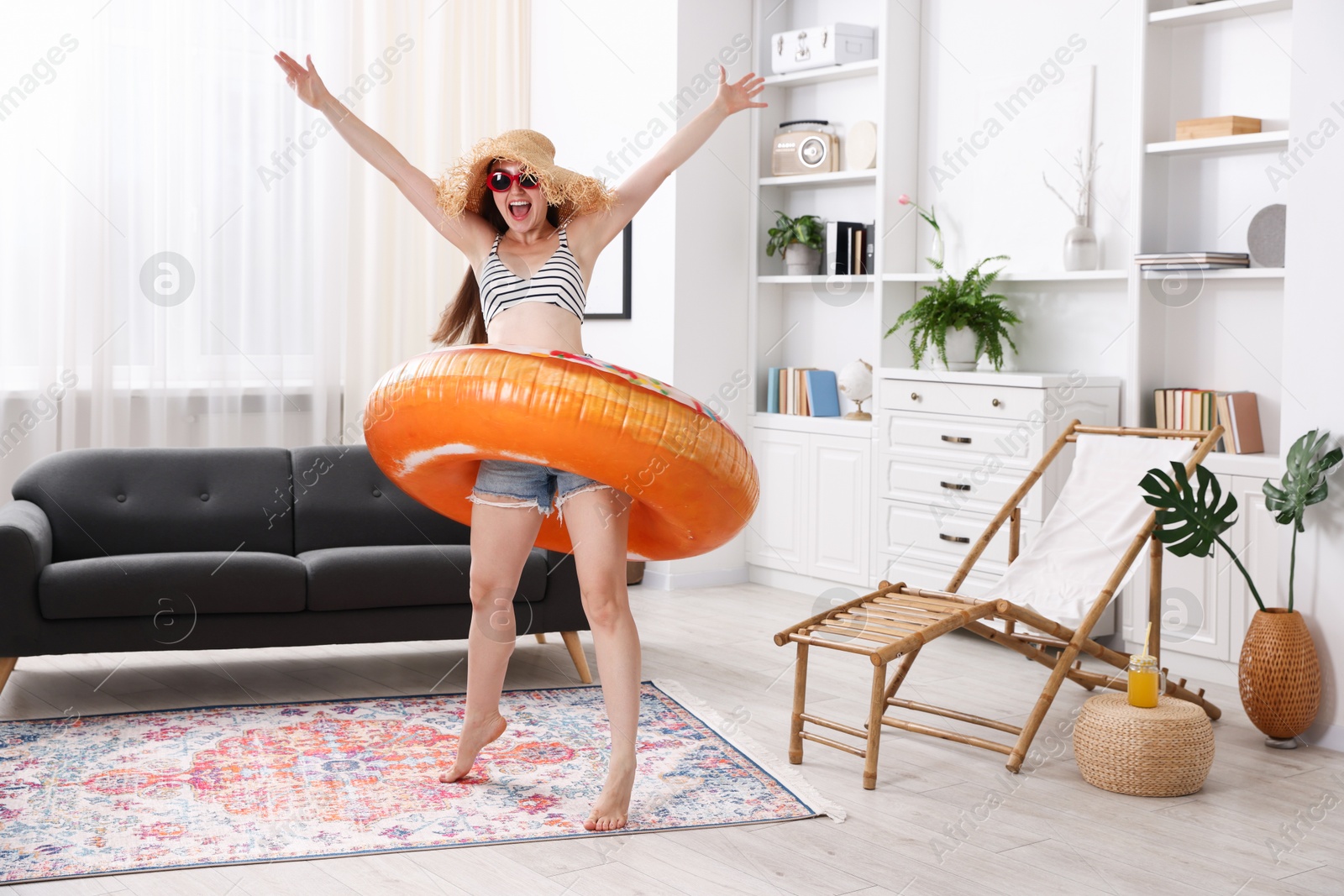 Happy woman in sunglasses and straw hat with inflatable ring having fun at home. Dreaming about vacation at sea Photo of Happy woman in sunglasses and straw hat with inflatable ring having fun at home. Dreaming about vacation at sea