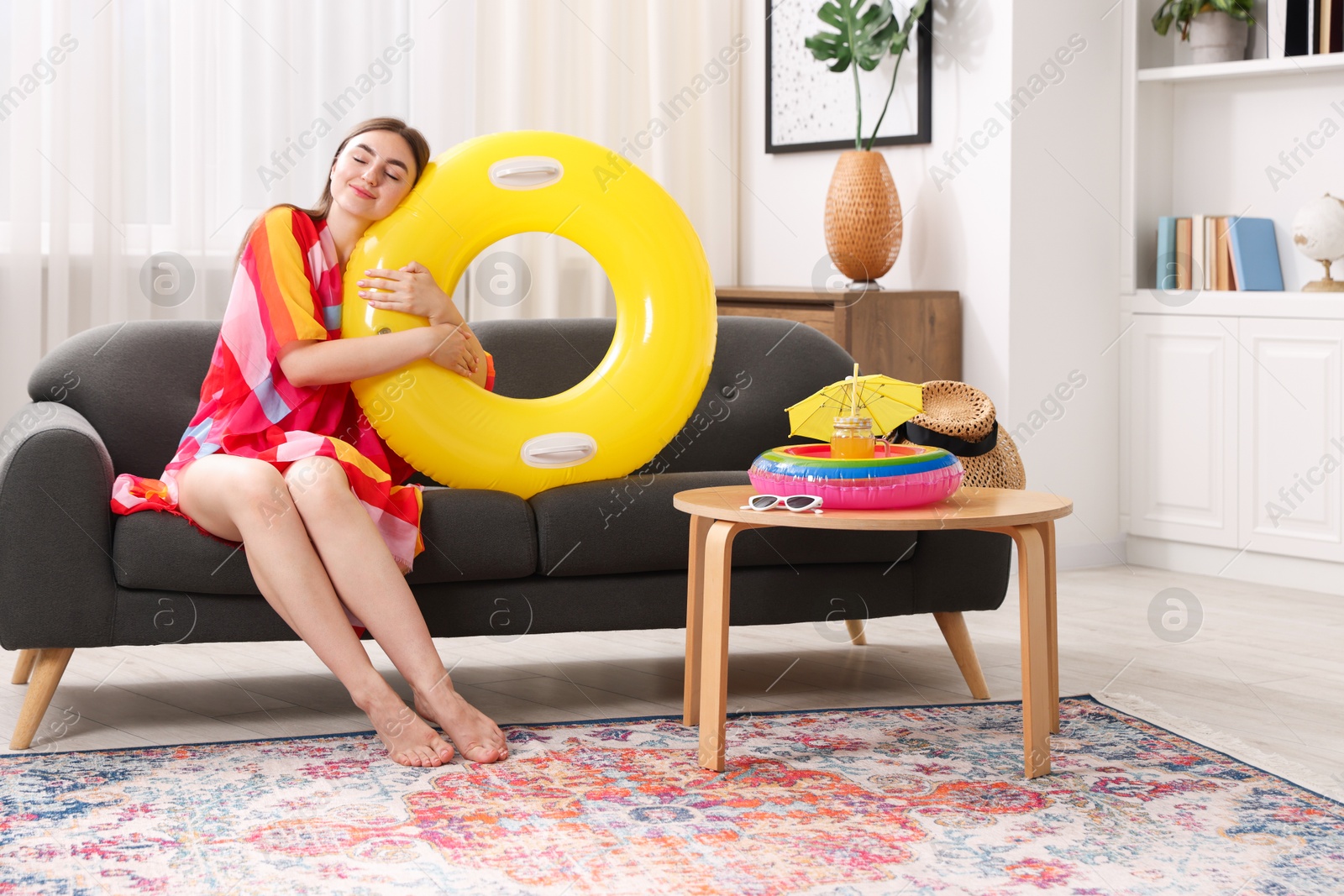Photo of Woman covered with pareo hugging inflatable ring on sofa at home. Dreaming about vacation at sea