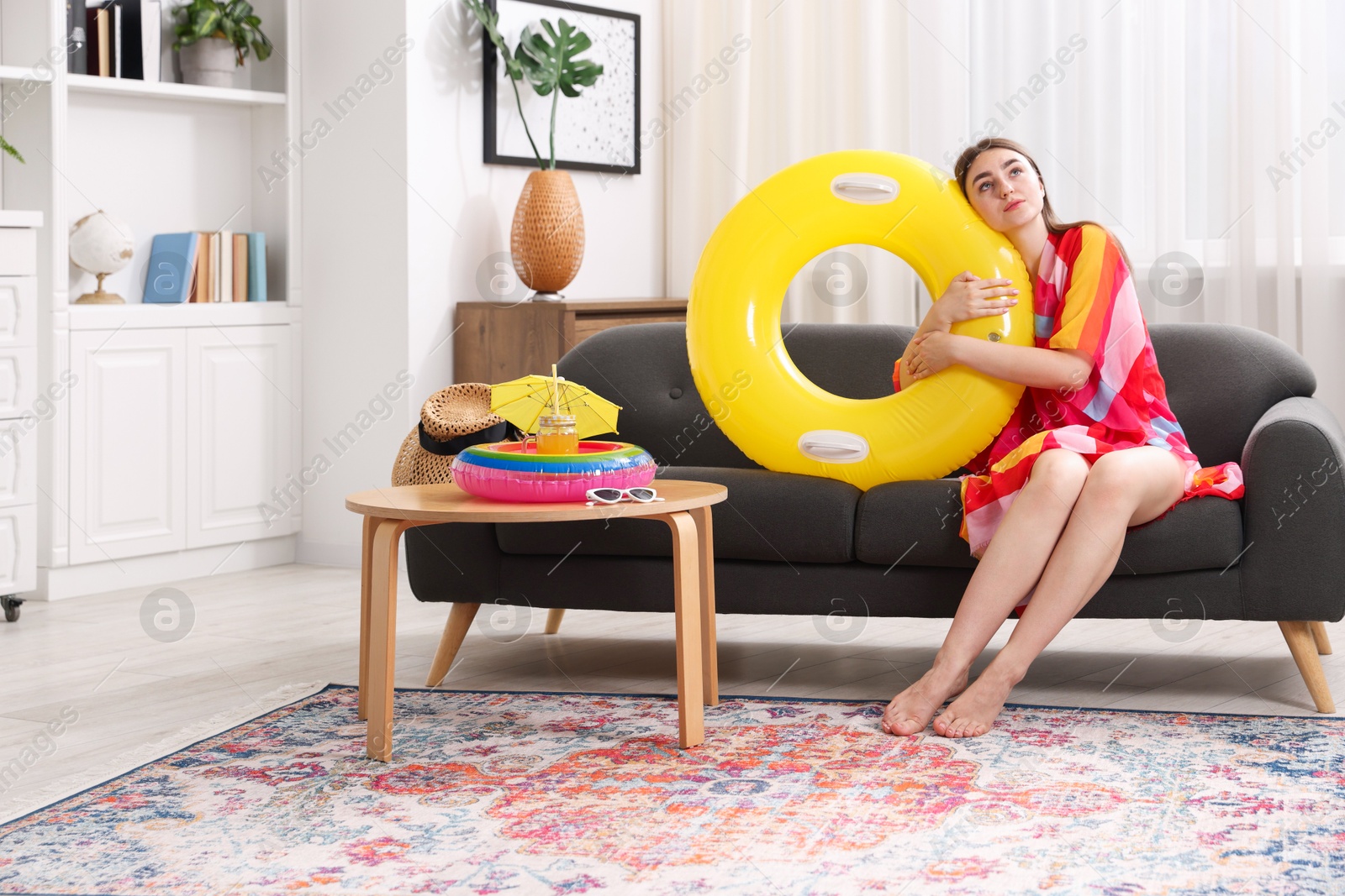 Photo of Woman covered with pareo hugging inflatable ring on sofa at home. Dreaming about vacation at sea