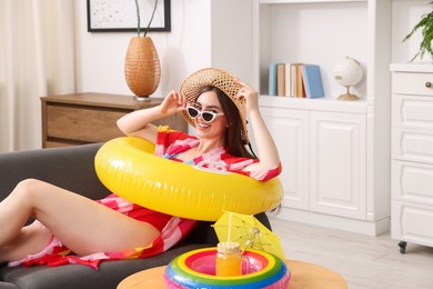 Photo of Happy woman in sunglasses and straw hat with inflatable ring having fun on sofa at home. Dreaming about vacation at sea