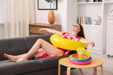 Photo of Woman in sunglasses with inflatable ring having fun on sofa at home. Dreaming about vacation at sea