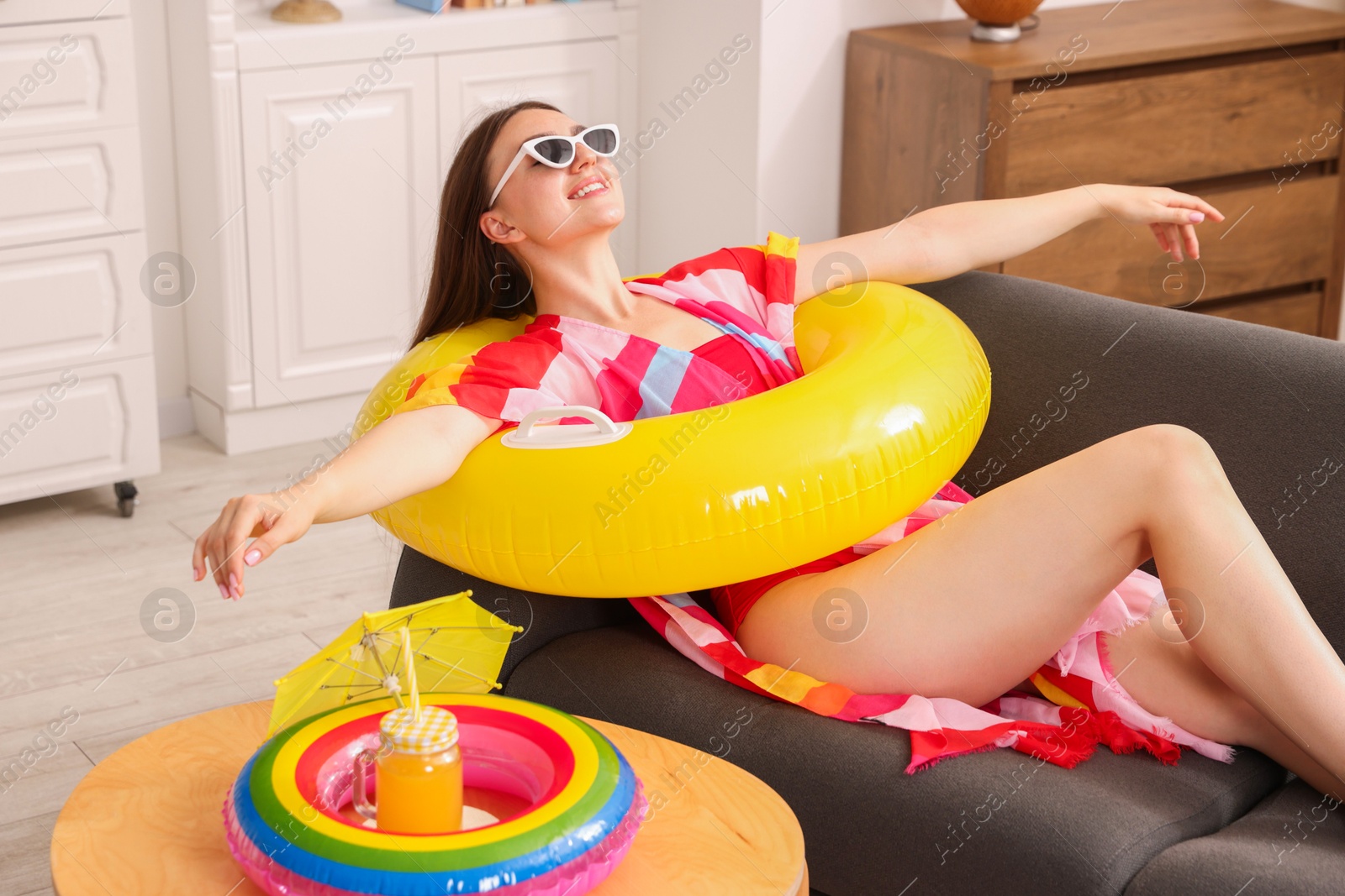 Happy woman in sunglasses with inflatable ring having fun on sofa at home. Dreaming about vacation at sea Photo of Happy woman in sunglasses with inflatable ring having fun on sofa at home. Dreaming about vacation at sea