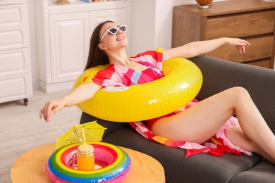 Photo of Happy woman in sunglasses with inflatable ring having fun on sofa at home. Dreaming about vacation at sea