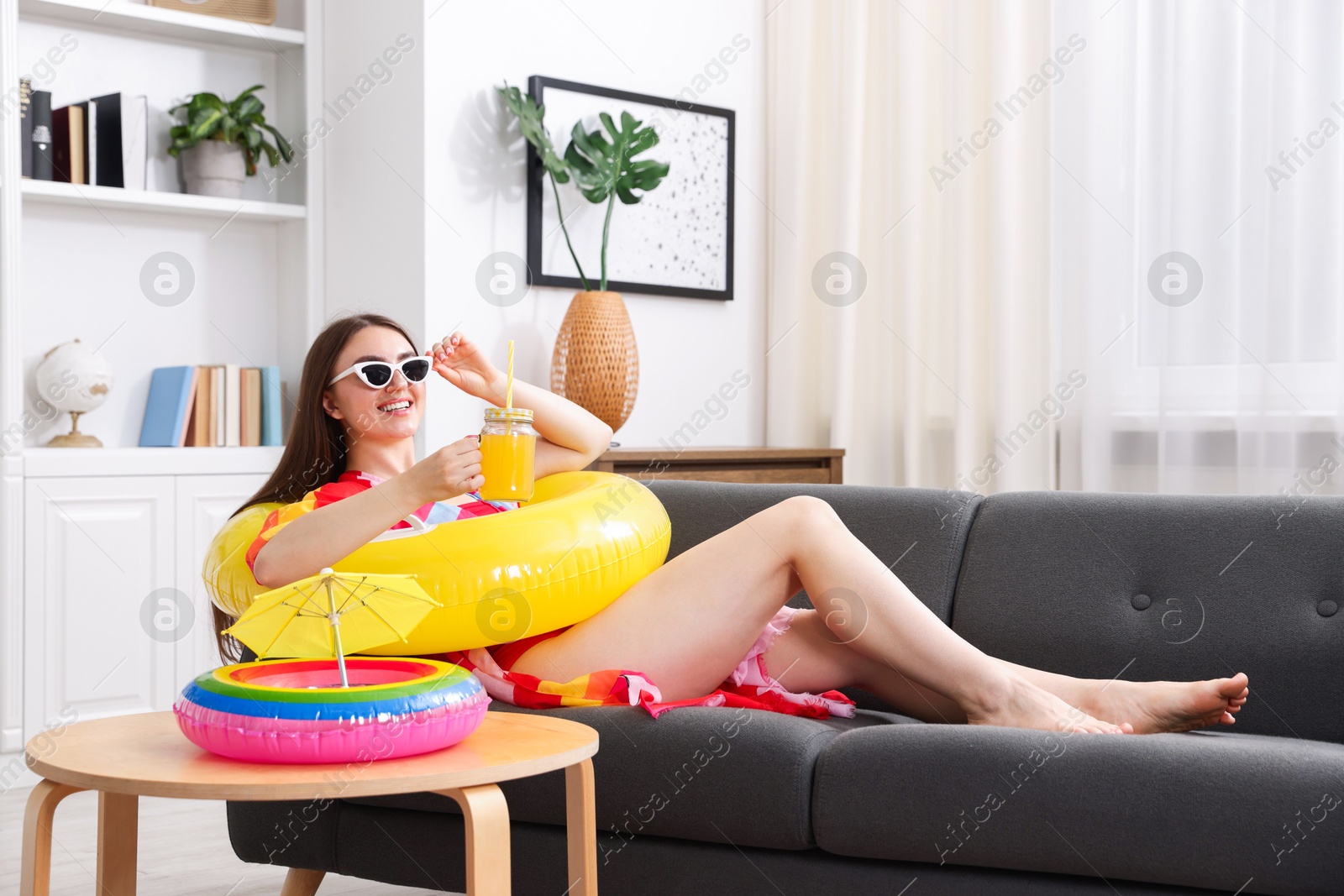 Happy woman in sunglasses with mason jar of juice and inflatable ring on sofa at home. Dreaming about vacation at sea Photo of Happy woman in sunglasses with mason jar of juice and inflatable ring on sofa at home. Dreaming about vacation at sea