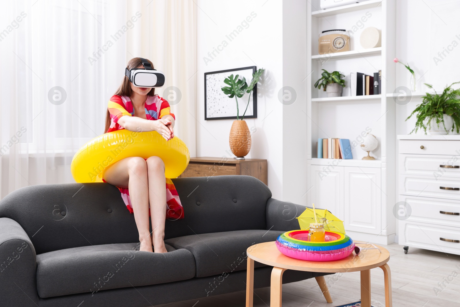 Woman with inflatable ring using virtual reality headset on sofa at home. Dreaming about vacation at sea Photo of Woman with inflatable ring using virtual reality headset on sofa at home. Dreaming about vacation at sea