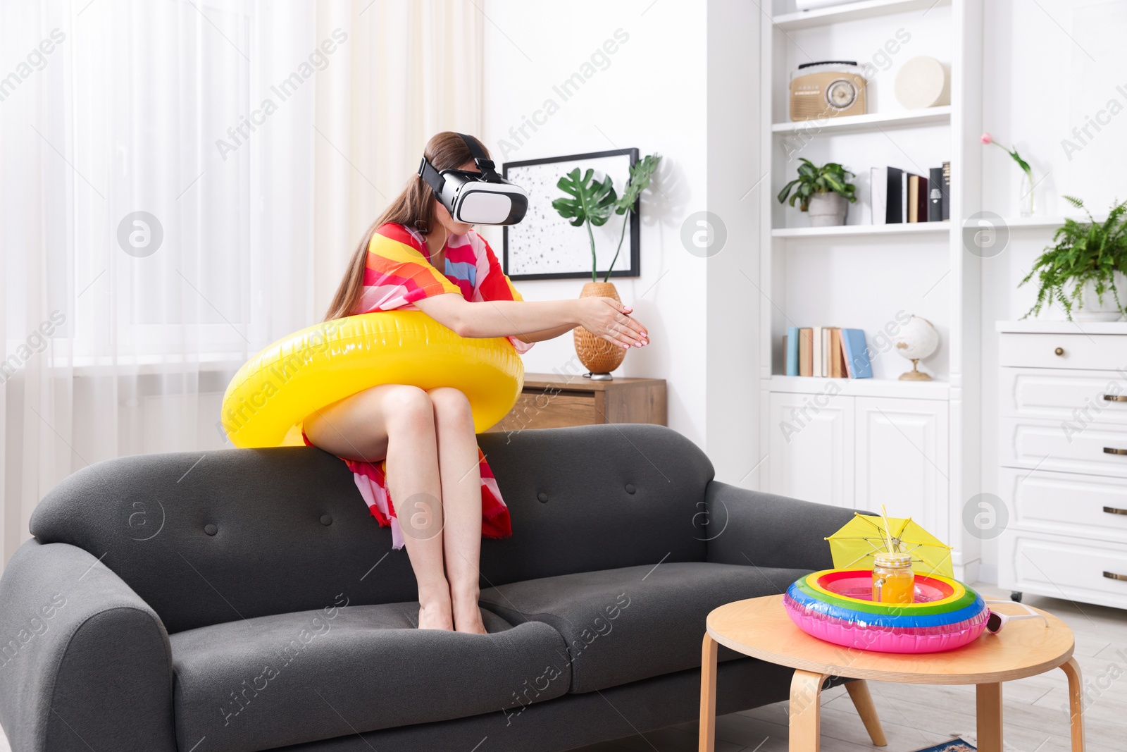 Woman with inflatable ring using virtual reality headset on sofa at home. Dreaming about vacation at sea Photo of Woman with inflatable ring using virtual reality headset on sofa at home. Dreaming about vacation at sea