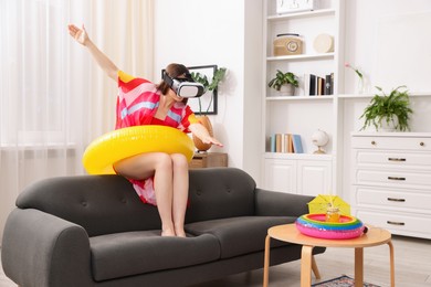 Photo of Woman with inflatable ring using virtual reality headset on sofa at home. Dreaming about vacation at sea
