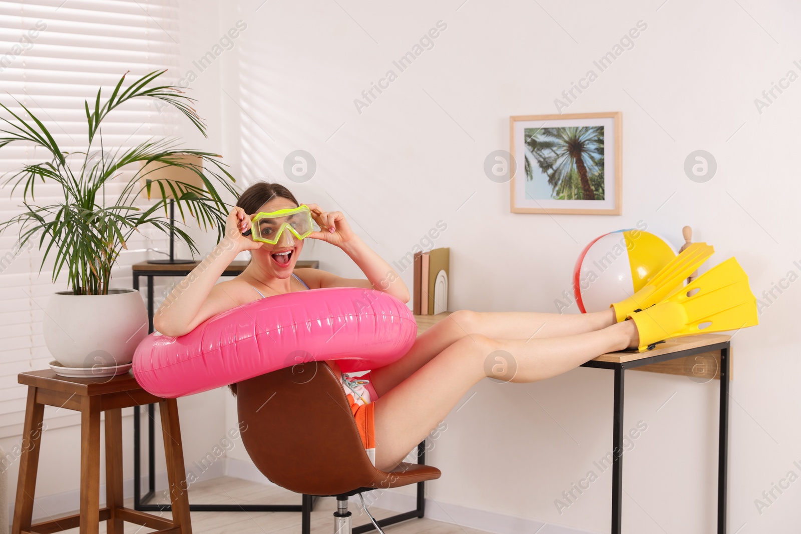 Happy woman in diving mask and flippers with inflatable ring on chair at home. Dreaming about vacation at sea Photo of Happy woman in diving mask and flippers with inflatable ring on chair at home. Dreaming about vacation at sea