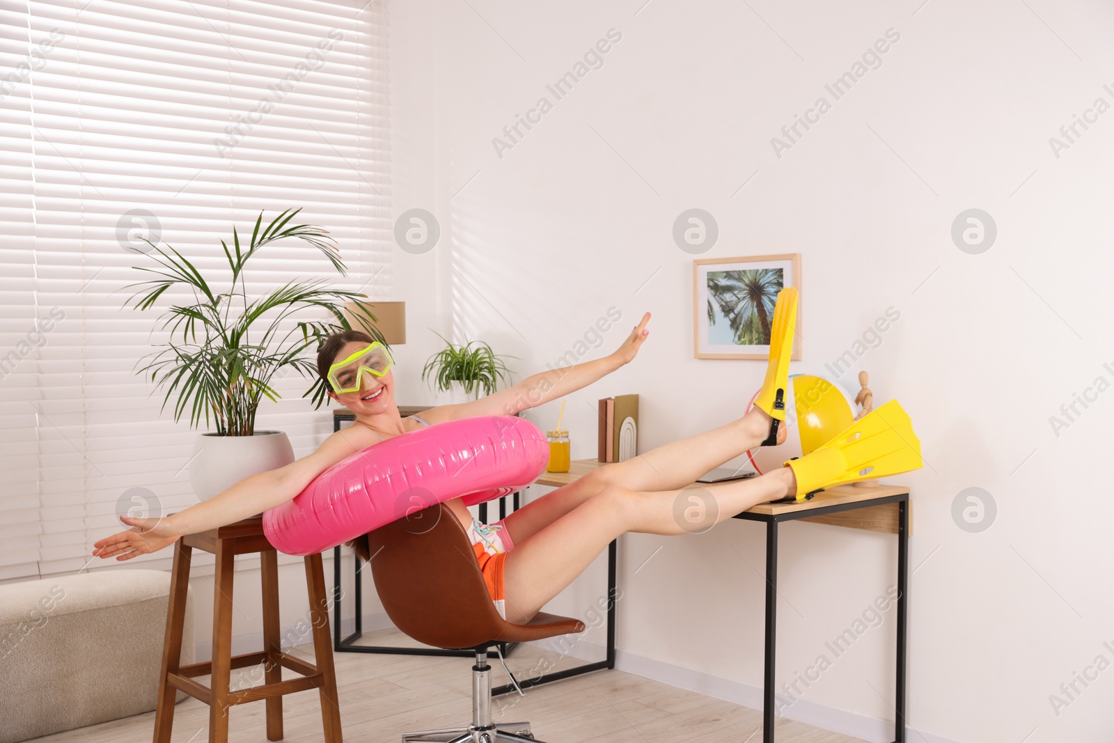 Happy woman in diving mask and flippers with inflatable ring on chair at home. Dreaming about vacation at sea Photo of Happy woman in diving mask and flippers with inflatable ring on chair at home. Dreaming about vacation at sea