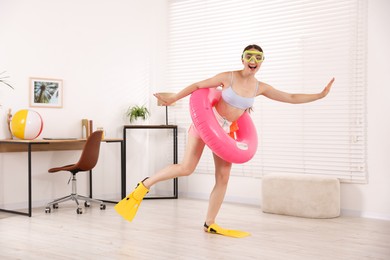 Photo of Happy woman in diving mask and flippers with inflatable ring having fun at home. Dreaming about vacation at sea