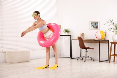 Photo of Woman in diving mask and flippers with inflatable ring having fun at home. Dreaming about vacation at sea