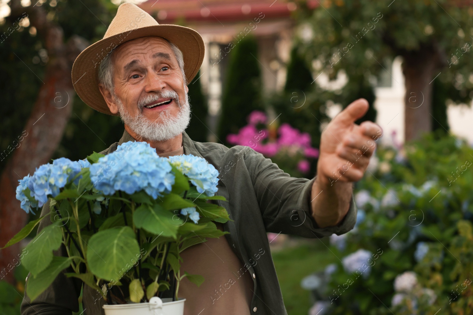 Photo of Smiling elderly man in hat with potted flowers in garden