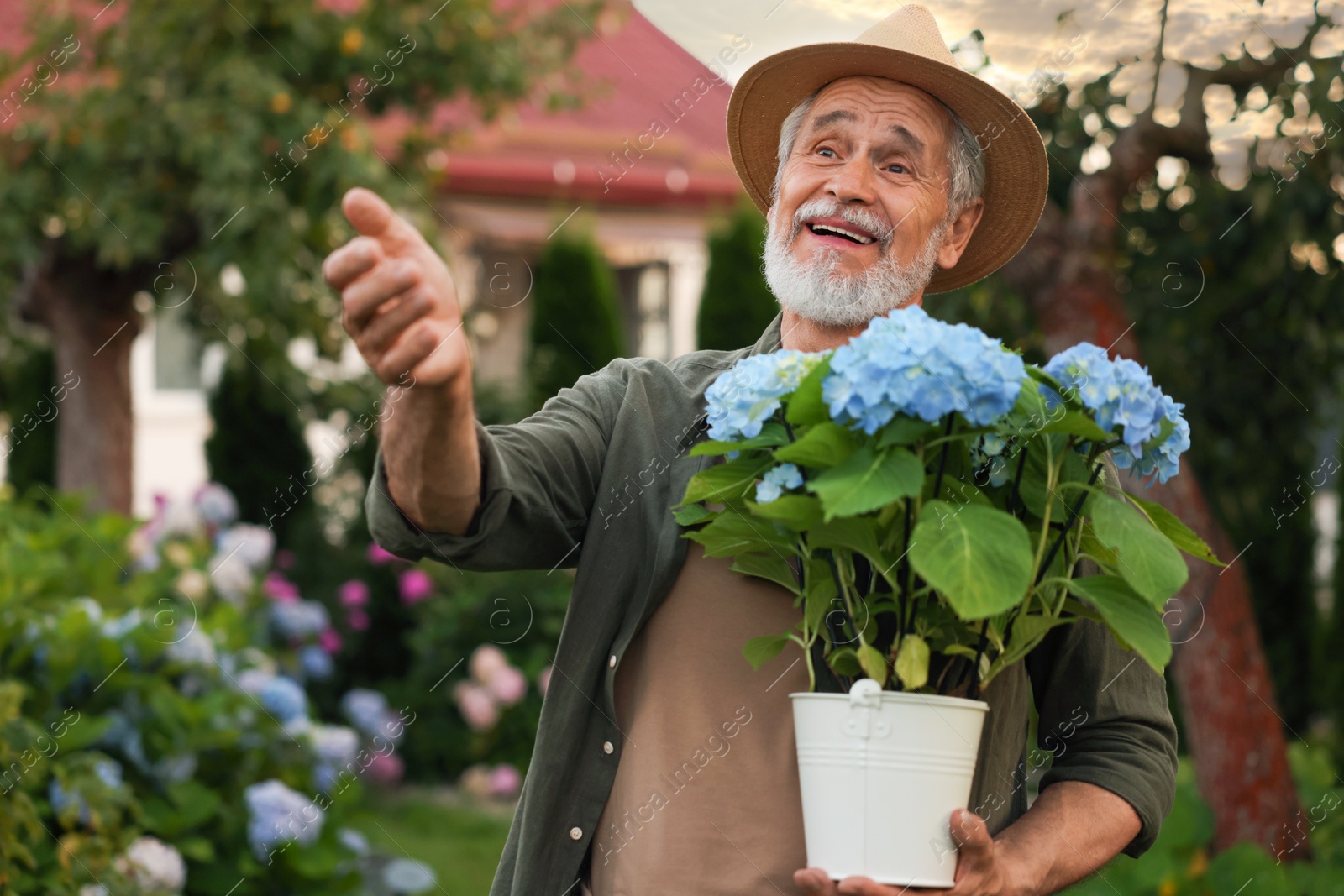 Photo of Smiling elderly man in hat with potted flowers in garden