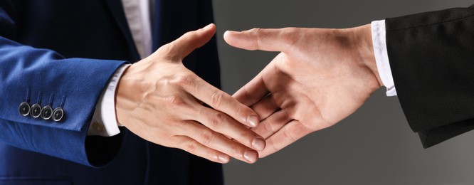 Photo of Business partners shaking hands on grey background, closeup