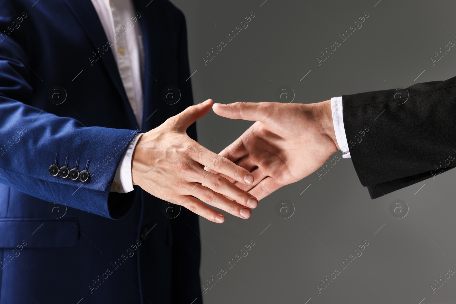 Business partners shaking hands on grey background, closeup Photo of Business partners shaking hands on grey background, closeup
