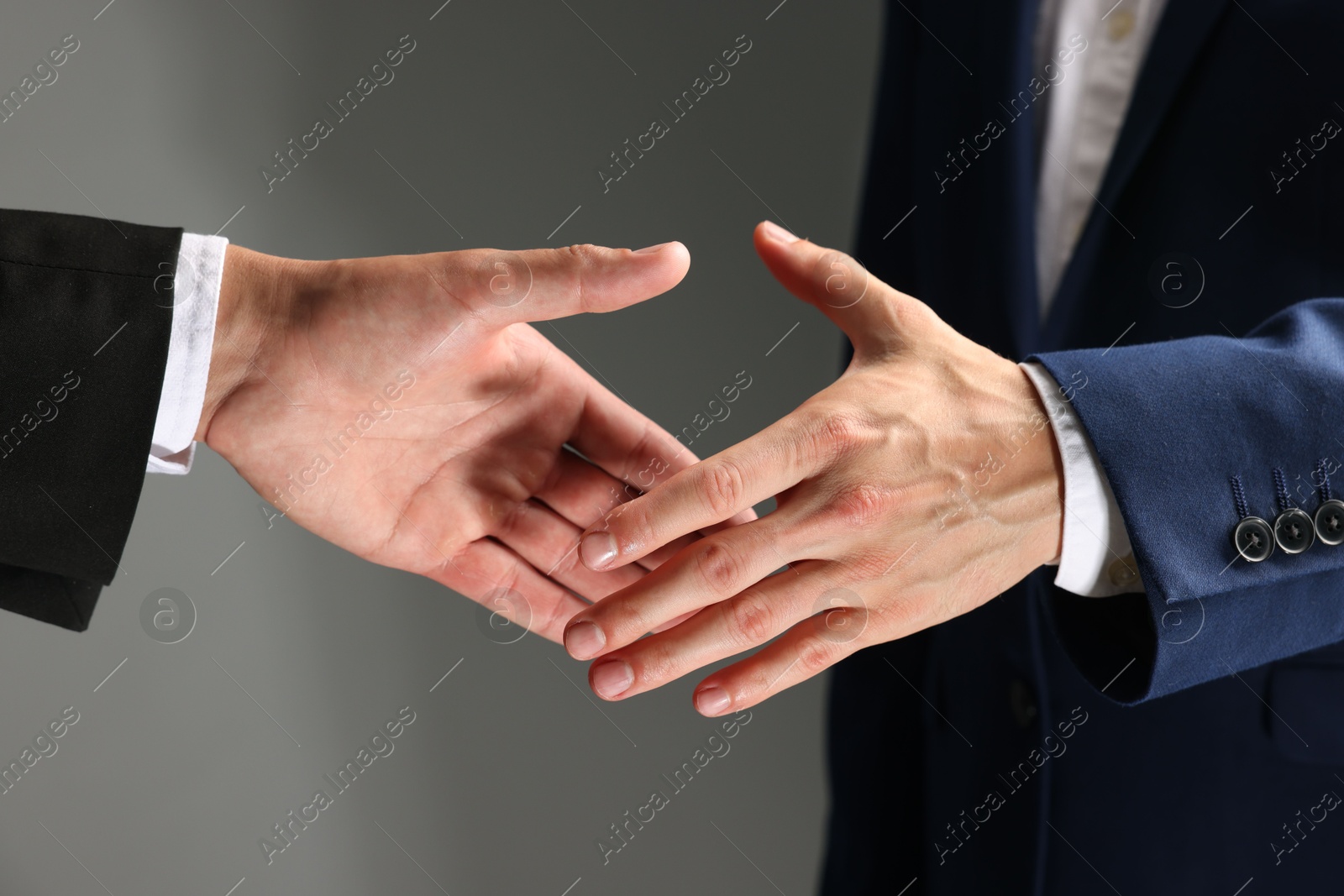 Business partners shaking hands on grey background, closeup Photo of Business partners shaking hands on grey background, closeup