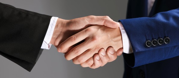 Photo of Business partners shaking hands on grey background, closeup