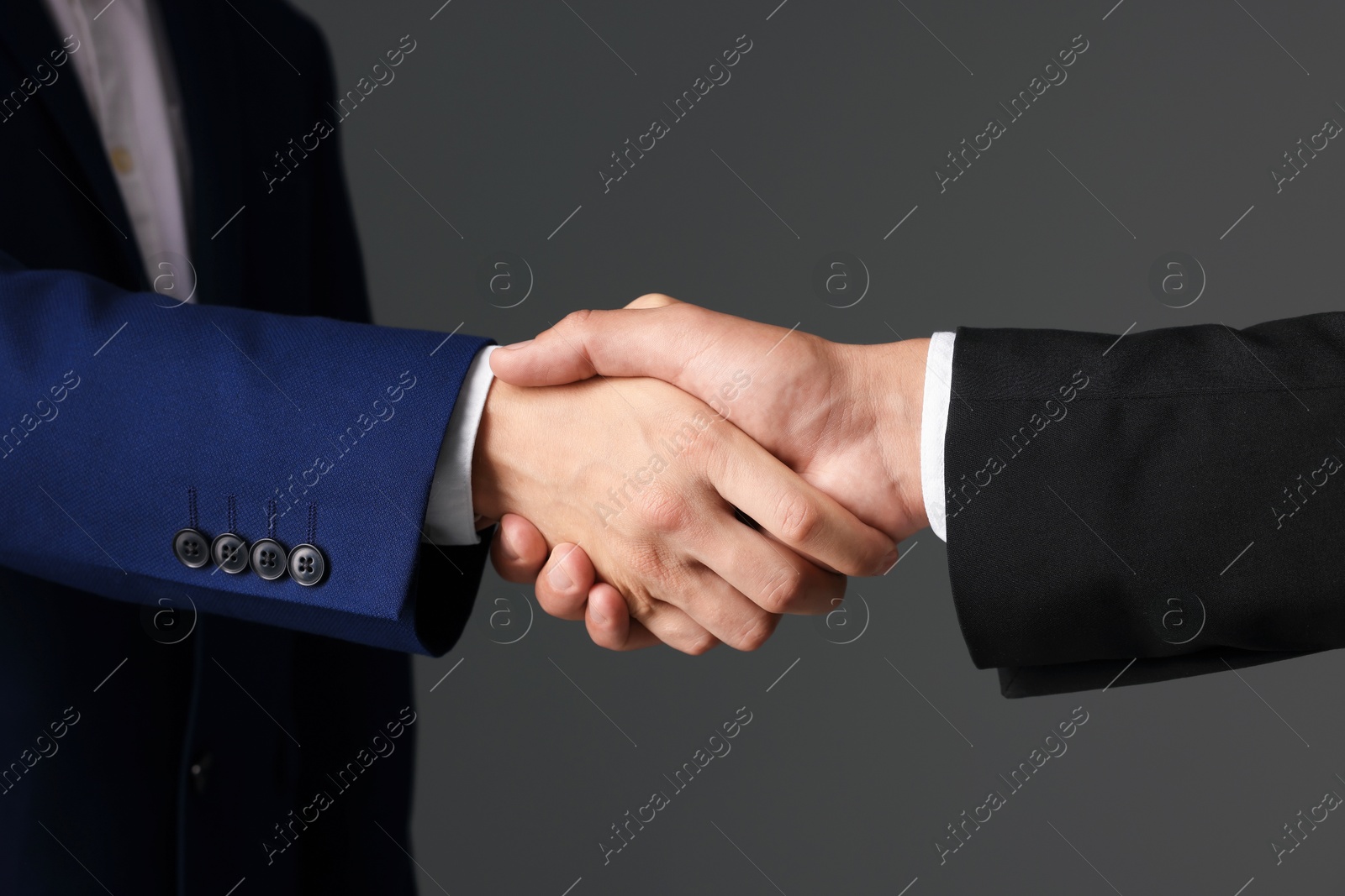 Business partners shaking hands on grey background, closeup Photo of Business partners shaking hands on grey background, closeup