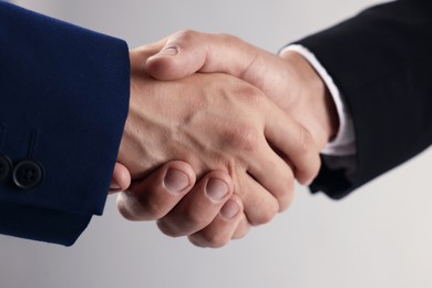 Photo of Business partners shaking hands on light grey background, closeup