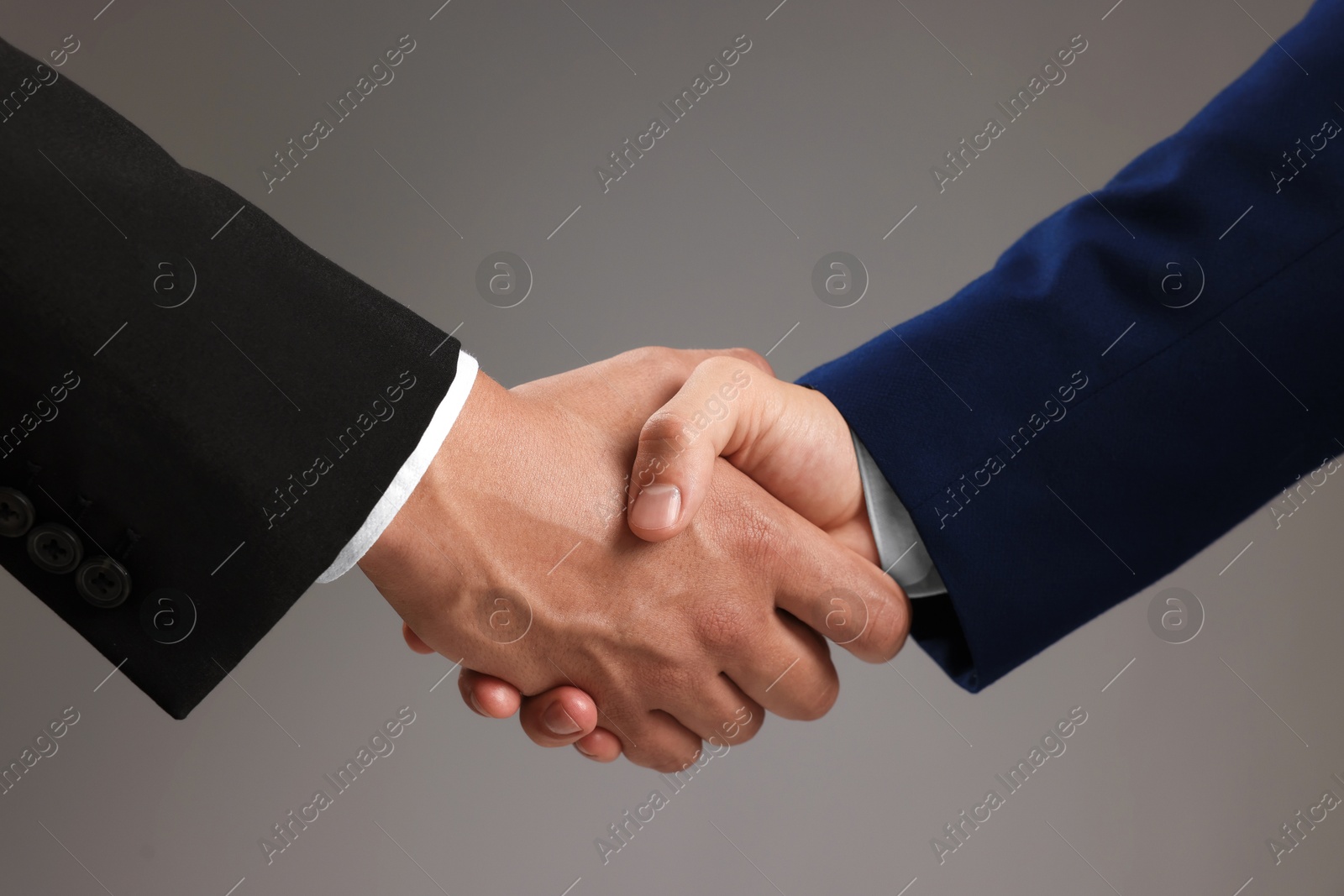 Business partners shaking hands on grey background, closeup Photo of Business partners shaking hands on grey background, closeup