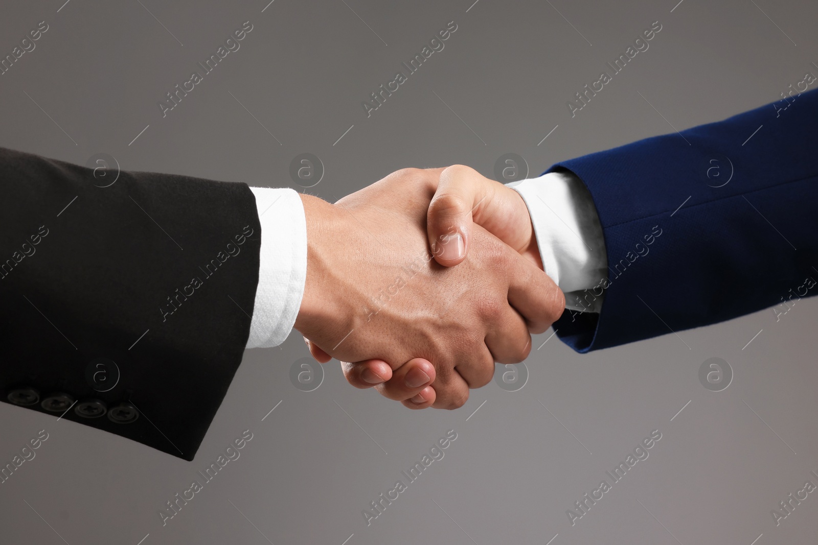 Business partners shaking hands on grey background, closeup Photo of Business partners shaking hands on grey background, closeup