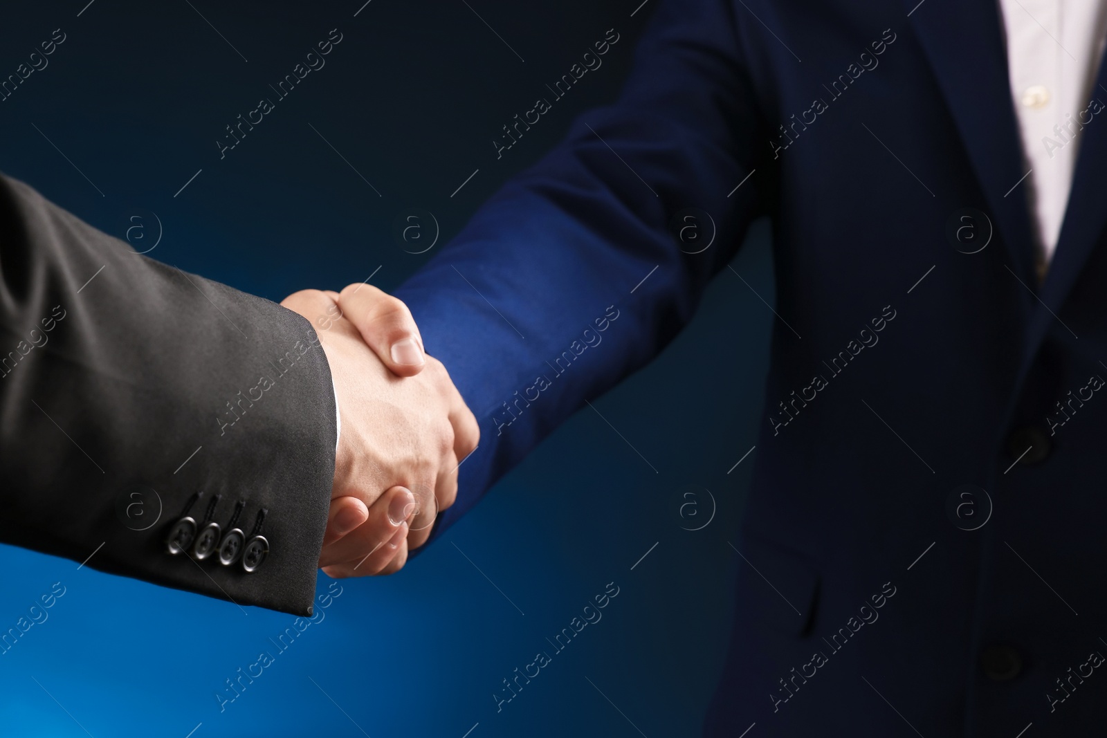 Business partners shaking hands on dark blue background, closeup Photo of Business partners shaking hands on dark blue background, closeup