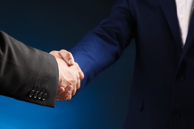 Photo of Business partners shaking hands on dark blue background, closeup