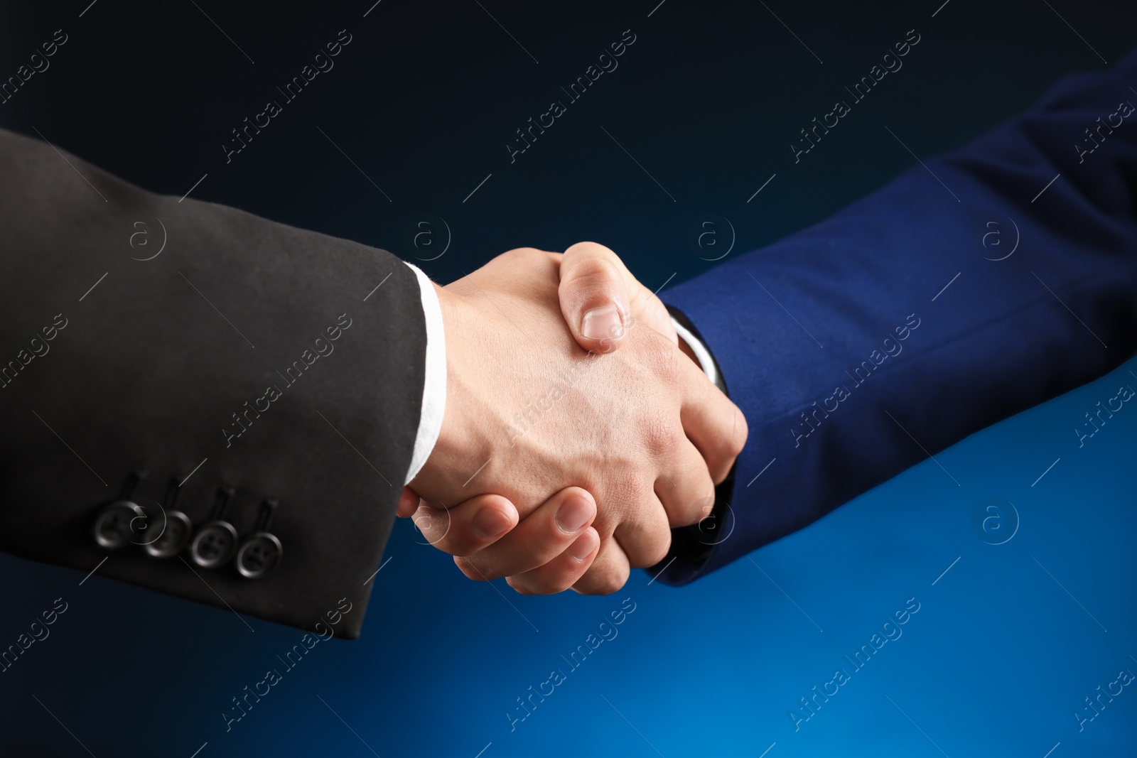 Business partners shaking hands on dark blue background, closeup Photo of Business partners shaking hands on dark blue background, closeup