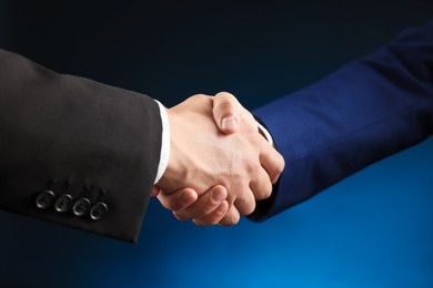 Photo of Business partners shaking hands on dark blue background, closeup