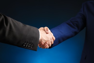 Photo of Business partners shaking hands on dark blue background, closeup