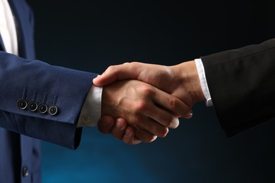 Photo of Business partners shaking hands on dark blue background, closeup