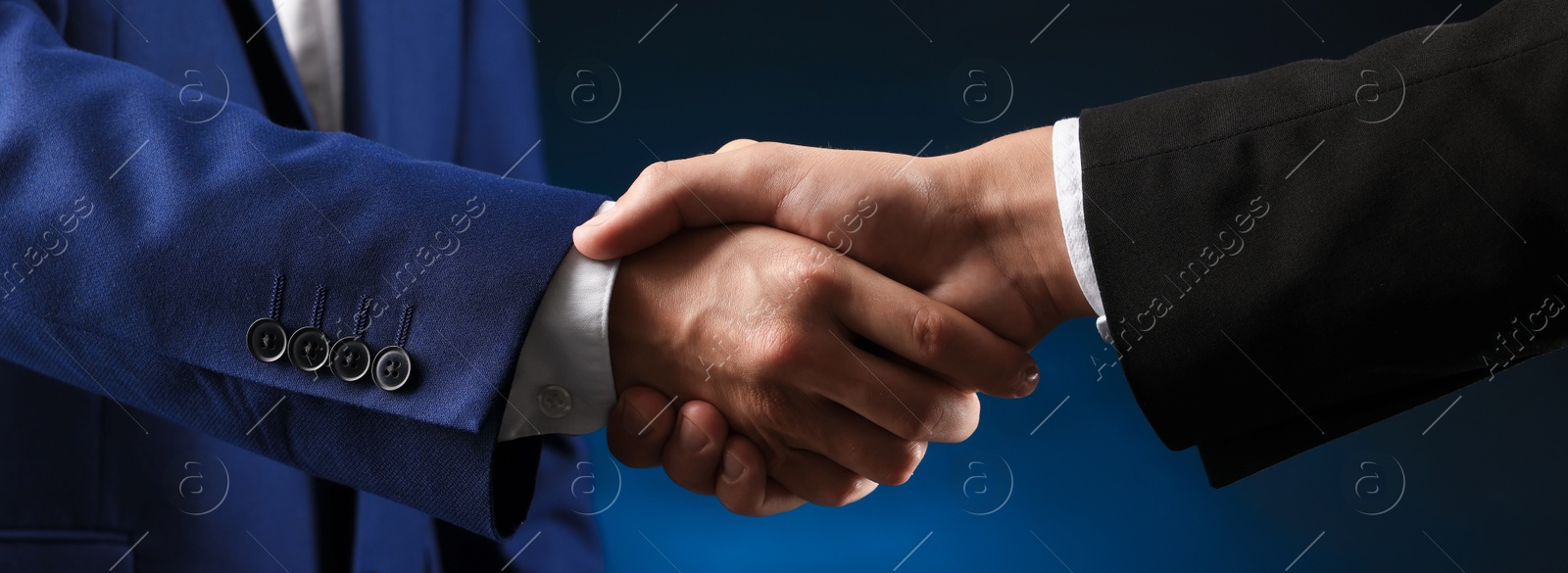 Photo of Business partners shaking hands on dark blue background, closeup