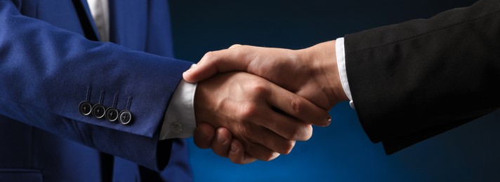 Photo of Business partners shaking hands on dark blue background, closeup