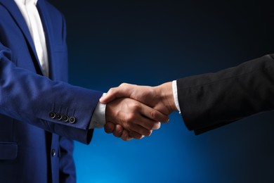 Photo of Business partners shaking hands on dark blue background, closeup