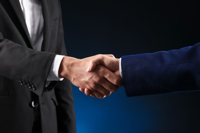 Photo of Business partners shaking hands on dark blue background, closeup