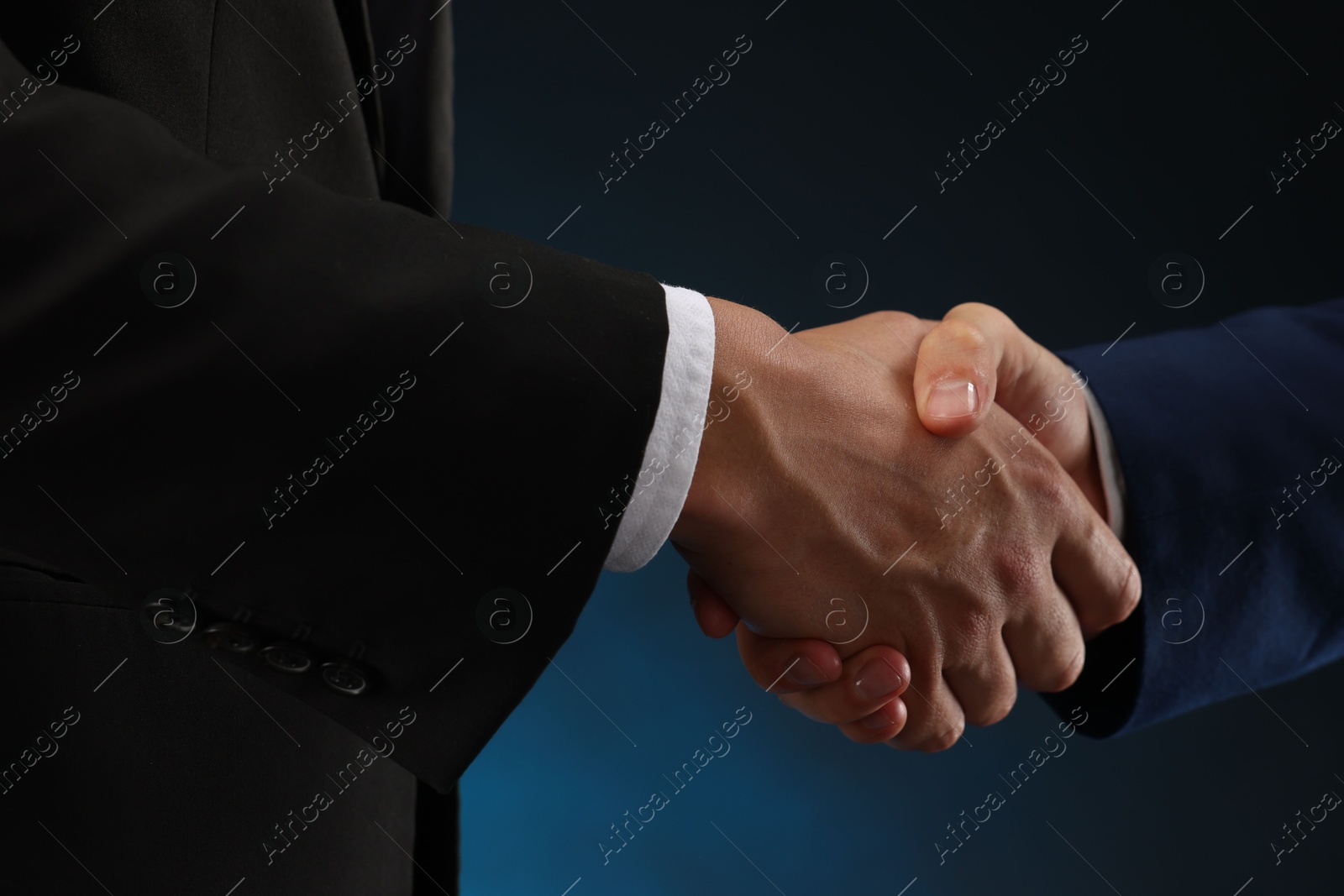 Business partners shaking hands on dark blue background, closeup Photo of Business partners shaking hands on dark blue background, closeup