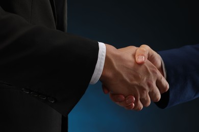Photo of Business partners shaking hands on dark blue background, closeup