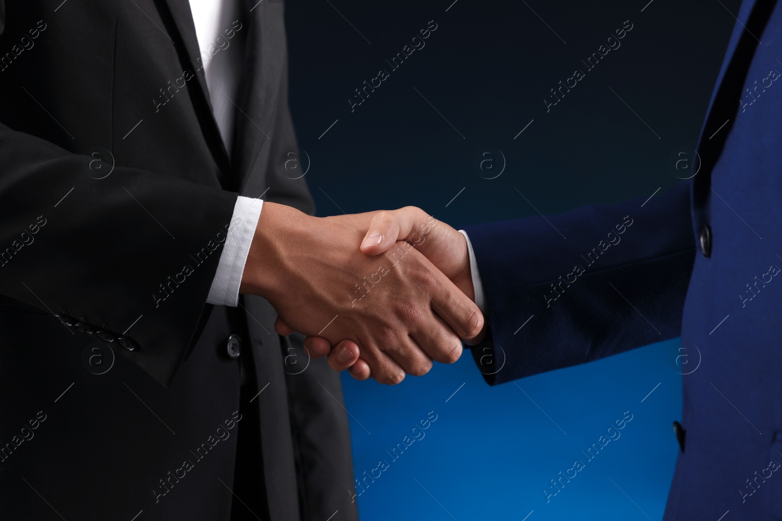 Business partners shaking hands on dark blue background, closeup Photo of Business partners shaking hands on dark blue background, closeup