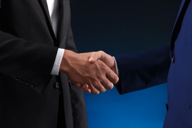 Photo of Business partners shaking hands on dark blue background, closeup